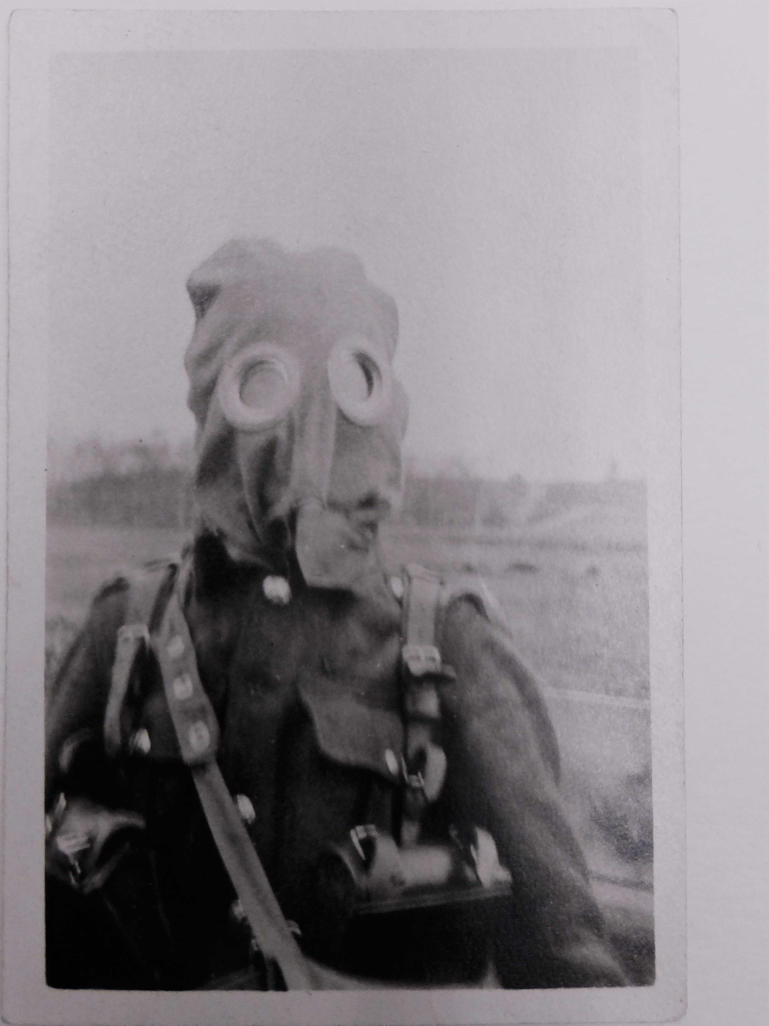 A black and white image of a soldier in military uniform wearing a primitive gas mask. The mask resembles a sack with two glass circles over top of his eyes.